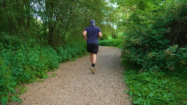 Middle aged man jogging through woodland park during fitness training. Recreational runner building endurance despite excess weight and physical effort. Healthy lifestyle, weight loss journey, outdoor