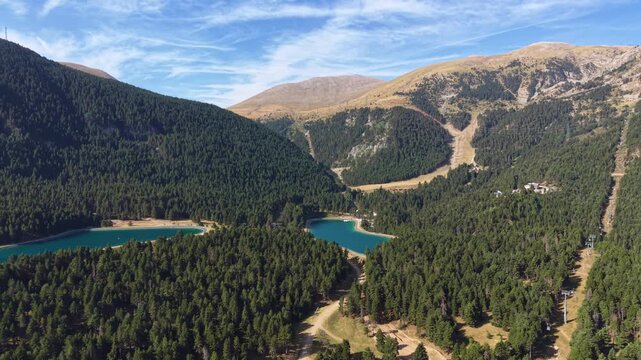 Aerial view of turquoise mountain lakes nestled among dense pine forests in La Molina ski resort, Catalan Pyrenees, Spain, with alpine meadows and ski slopes in background