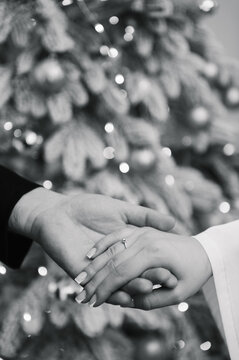 Marriage proposal, man holding woman's hand wearing a diamond engagement ring. Black and white photo. Festive blurred background with bokeh lights. Romantic moment, love, engagement, promise. Closeup