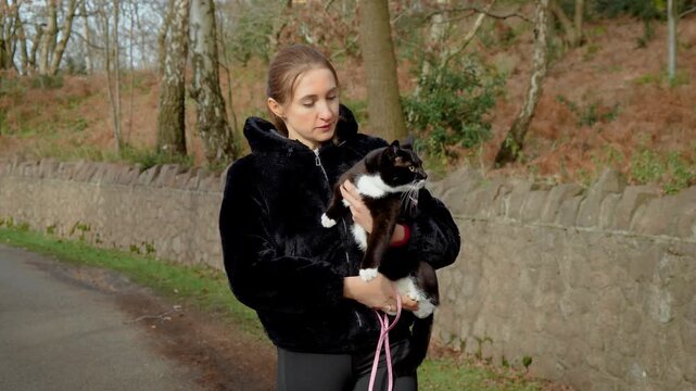 Affectionate woman walking along countryside road holding domestic cat close. Loving pet owner embracing black and white feline, nurturing gentle interaction and trust. Sharing warmth and emotional