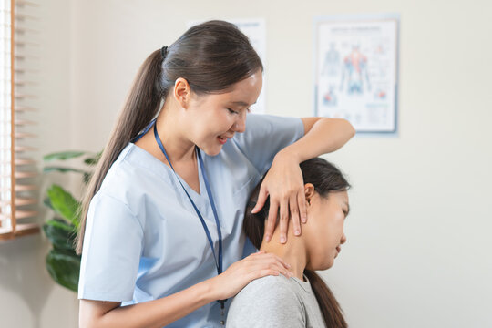 Professional Asian female physiotherapist treating young woman with neck pain stretching muscle in physical therapy clinic wellness health care concept