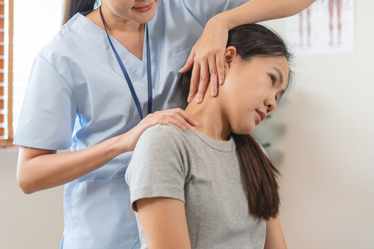 Professional Asian female physiotherapist treating young woman with neck pain stretching muscle in physical therapy clinic wellness health care concept
