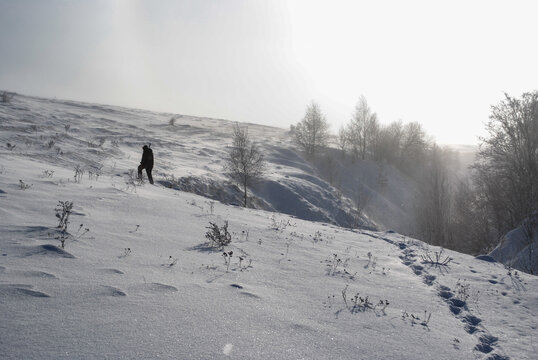 A hunter with a shotgun stands on a snow-covered hill next to a deep ravine on a sunny winter day.