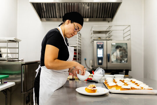 A pastry chef between 30 and 40 years old, wearing a hat and apron, is making cakes in a modern bakery.The woman is finishing a cake.Concept of Mexican cooks.