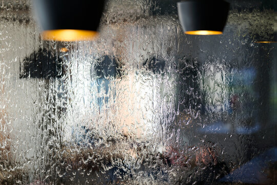 Wet Window With Blurred Cafe Interior and Hanging Lamps Through Rain Soaked Glass