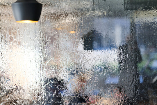 Rain-Soaked Window Overlooking Blurred Cafe Interior With Warm Pendant Lamp And People