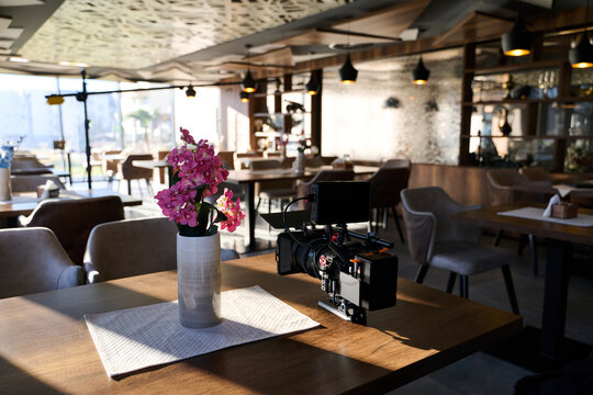 Professional Cinema Camera Filming Flowers in Vase on Table at Sunlit Modern Cafe Interior
