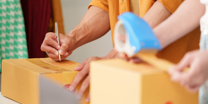Ecommerce small business team sealing cardboard boxes and writing shipping labels for parcel delivery