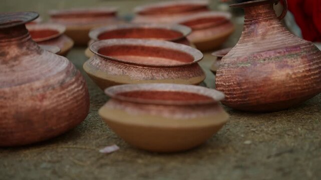 A row of hand hammered copper bowls sits on bare ground with one bowl in sharp focus surrounded by softly blurred matching vessels