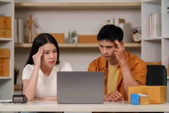 Stressed Asian small business couple looking at laptop while analyzing digital data and ecommerce challenges