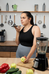 Fit woman recording voicemail about healthy eating at smartphone in kitchen