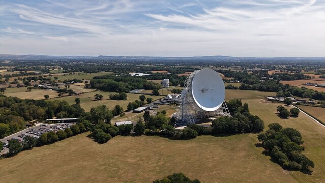 Cheshire, United Kingdom - 08 August 2026: Aerial view of the Lovell Telescope at Jodrell Bank Centre for Engagement, surrounded by rural fields, trees, and parking under a blue sky.