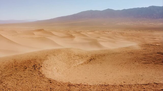 Sand Dunes in Desert Landscape with Wind Blowing Across Sandy Terrain and Distant Mountains Under Clear Sky and Arid Environment