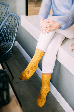Comforting cozy woman in knitted woolen winter yellow socks, white trousers and blue warm sweater resting sitting on a bench at cafe in winter time. Cozy time