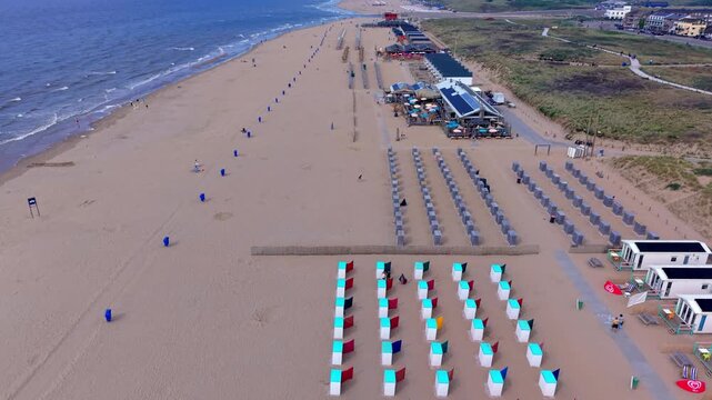 Aerial view video clip of Katwijk aan Zee beach resort, colorful beach cabins, windbreaks, modern beach houses, coastal sand dunes, town skyline, and North Sea in South Holland, Netherlands