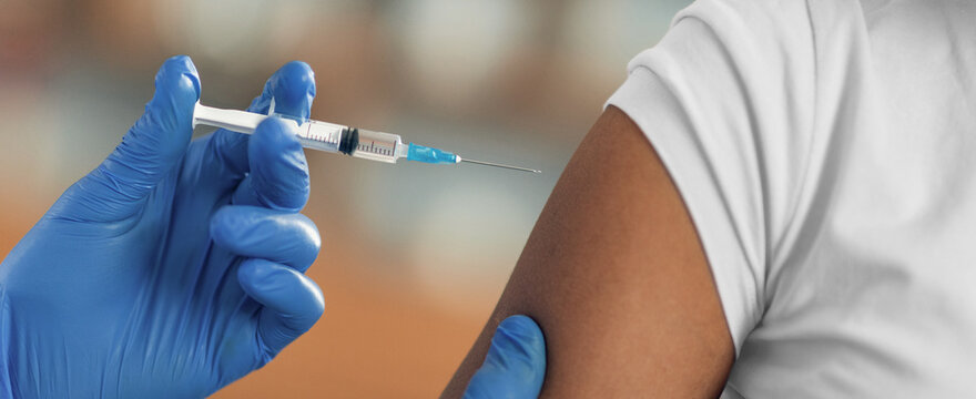 Focused Black Male Patient Receiving Vaccine Injection By Professional Healthcare Worker In Clinic Setting. Procedure Ensures Patient Health And Safety During Vaccination Process. Healthcare Concept.