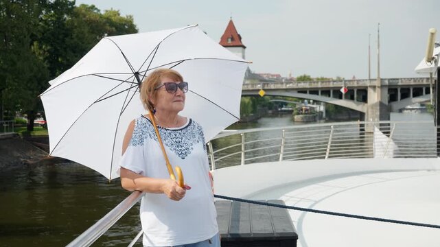 Senior woman enjoys a scenic riverboat cruise through historic Prague. She views urban landmarks along the Vltava embankment. Active European vacation offers comfortable summer city tourism.