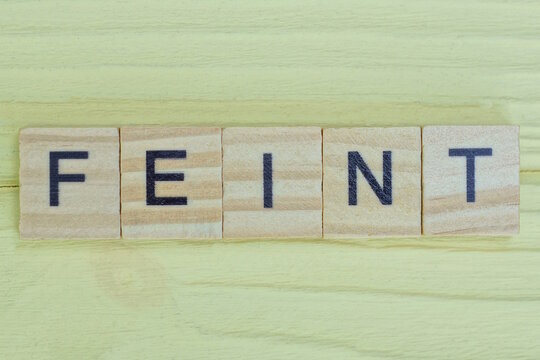 the gray word feint of gray small wooden letters lie on a yellow table