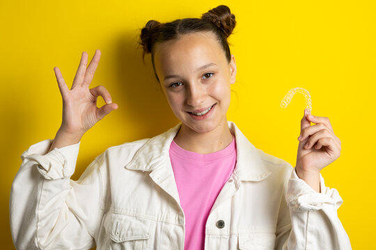 Teenage girl Teenage girl smiling while holding a transparent dental aligner for teeth straightening. Adolescent orthodontics, invisible braces, dental care and oral health concept.holding clear denta