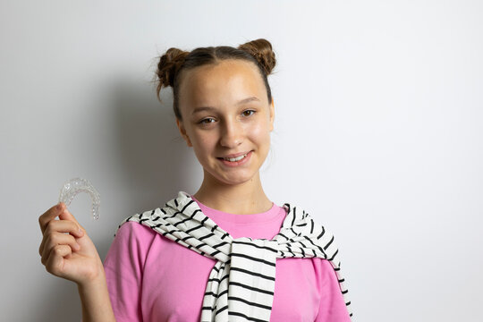 Teenage girl Teenage girl smiling while holding a transparent dental aligner for teeth straightening. Adolescent orthodontics, invisible braces, dental care and oral health concept.holding clear denta