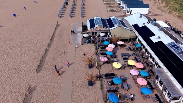 Aerial view video clip of Katwijk aan Zee beach resort, Surf Beach restaurant pavilion, colorful outdoor terrace umbrellas, paved boardwalk, and sandy shore in South Holland, Netherlands