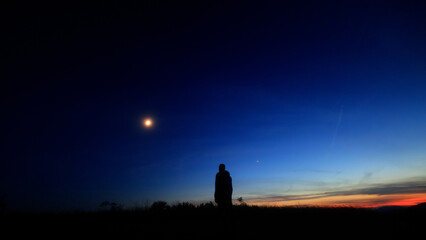Silhouette of a person in nature observing night sky, Moon, stars and planets from a remote location. © astrosystem