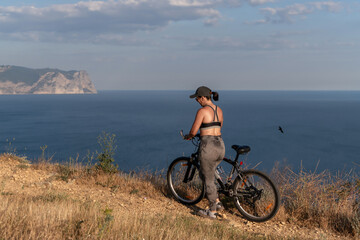 Fototapeta premium Bicycle travel woman standing on a cliff overlooking the sea while resting during an outdoor workout session in summer