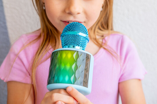 Close-up cute young girl pop star singing into toy microphone, wearing pink shirt, karaoke fun, childhood entertainment, performance, music hobby, Overcoming fear in children through public speaking