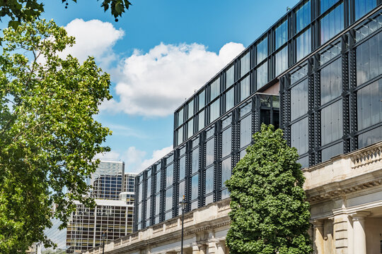View of the modern glass facade of a building integrated with classical stone architecture under a bright blue sky in Belgravia, London, England, United Kingdom.