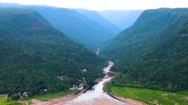 Dry hill river, winding river valley framed by steep, forest-covered Meghalaya hills near the Bangladesh India border area at Bichanakandi, high angle wide aerial drone shot, daytime, overcast light,