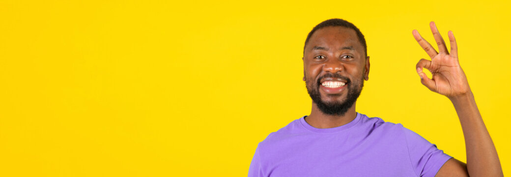 Smiling Black Man In His 30s Making Okay Gesture With Hand, Exuding Confidence And Positivity, Against A Bright Yellow Background, Ideal For Business Concept Or Lifestyle Imagery.
