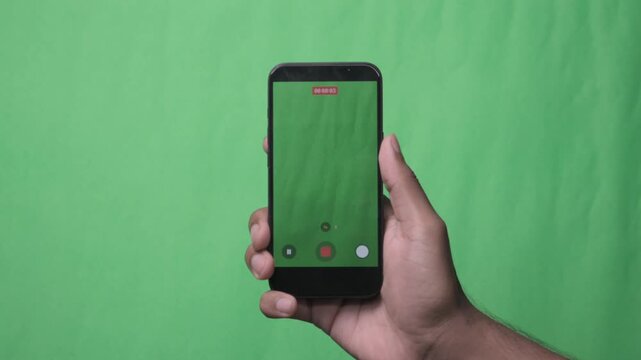 Hand Holding a Smartphone Against a Green Screen.