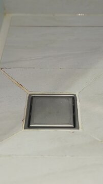 Stainless steel square floor drain in bathroom.
