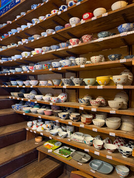 Traditional Japanese ceramic bowls and tableware displayed on wooden shelves in a pottery shop in Kappabashi, Tokyo, showcasing colorful patterns, handmade designs and Japanese craftsmanship