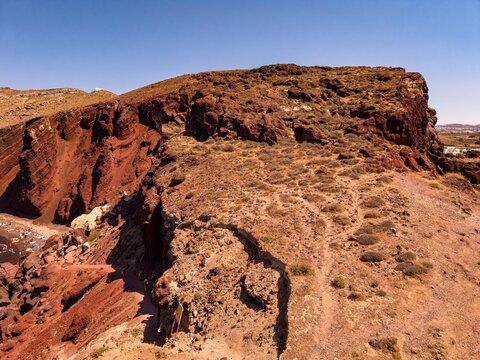 Aerial view of red volcanic cliffs and rock formations at Red Beach in Santorini Greece drone shot