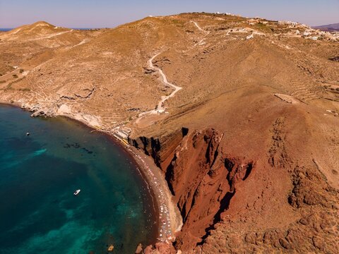Aerial view of dramatic red cliffs and clear blue bay at Red Beach in Santorini island Greece drone shot