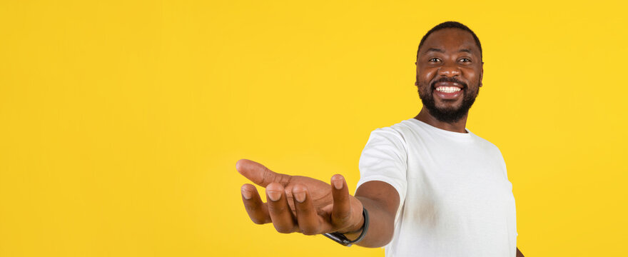 Smiling Black Man Extending Hand With Enthusiasm, Demonstrating Openness In Studio Environment With Bright Yellow Background. This Captures Positive Energy And Professionalism. Business Concept.