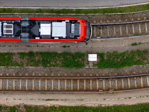 Aerial view of a red tram moving along tracks with gravel ballast and green grass in Gdansk, Poland.