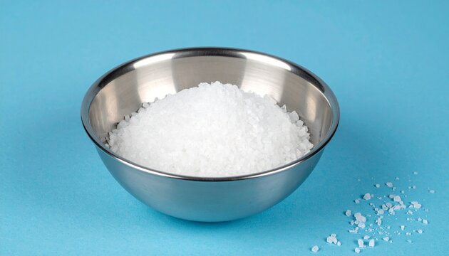 Metallic bowl of salt crystals, vivid blue background, purity
