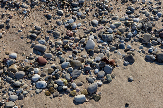 Pebbles on a calm beach sand by the sea in natural grey and brown tones