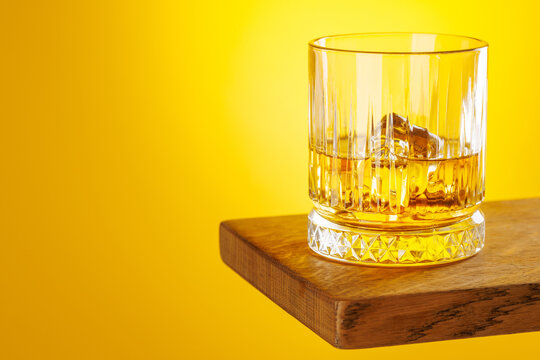 Whiskey glass with ice on yellow background minimal drink still life