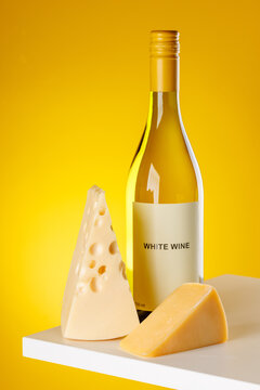 White wine with cheese pieces on yellow background gourmet composition