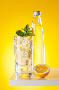 Sparkling water with lemon and bottle on yellow background refreshment