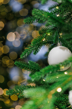 White Christmas ornament on fir tree with golden bokeh lights