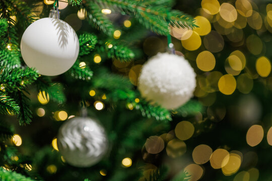 White Christmas ornament on fir tree with golden bokeh lights