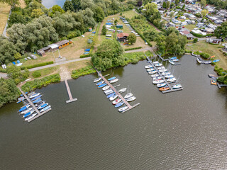 Naklejka premium Aerial view of a small marina with sailboats docked along the calm lakeside in a summer landscape.