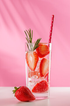 Fresh strawberry infused water with herbs on pink background with copy space