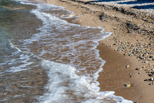 Wave lapping on sand, in beach, with sand, pebbles, from a top-down perspective, with brown, gray accents, and calm serene mood, with nearby objects, in surrounding setting.