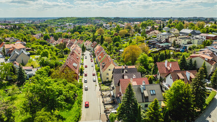 Aerial view of Ojcowska Street in Siedlce, Gdańsk, Poland, showing distinctive terraced houses surrounded by lush greenery and gardens. © Kamil