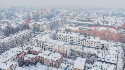 Aerial view of Dolne Miasto in Gdańsk, Poland, covered in snow, showing historic brick buildings, residential streets, industrial architecture and ongoing urban development. © Kamil
